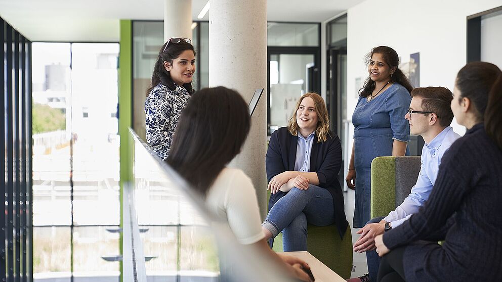 Fünf Frauen und ein Mann sitzen und stehen zusammen und unterhalten sich.